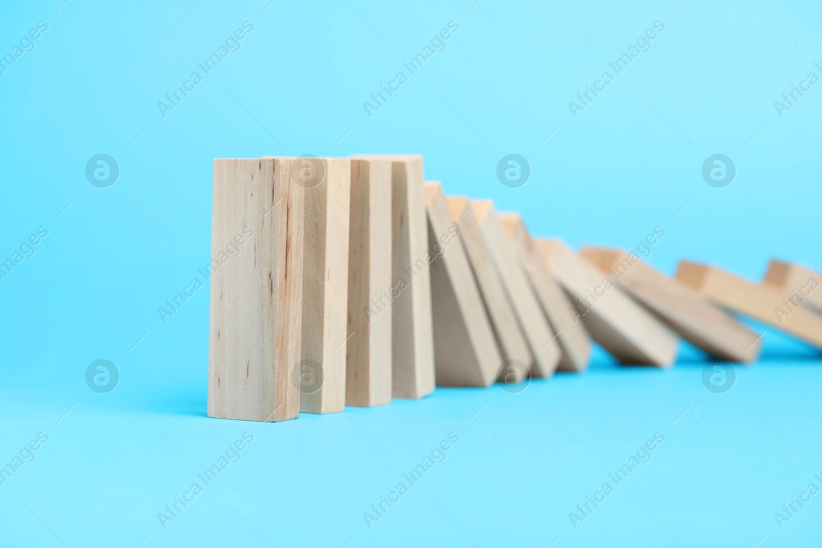 Photo of Domino effect. Wooden blocks falling on light blue background