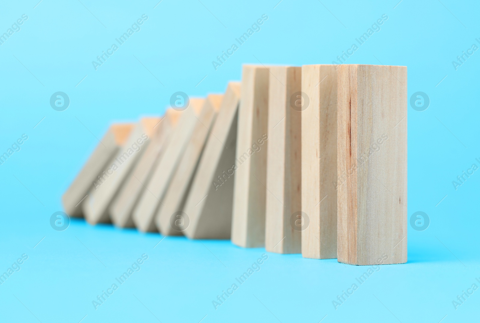 Photo of Domino effect. Wooden blocks falling on light blue background