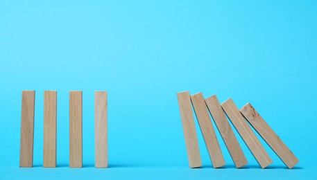 Photo of Domino effect. Wooden blocks falling on light blue background. Space for text