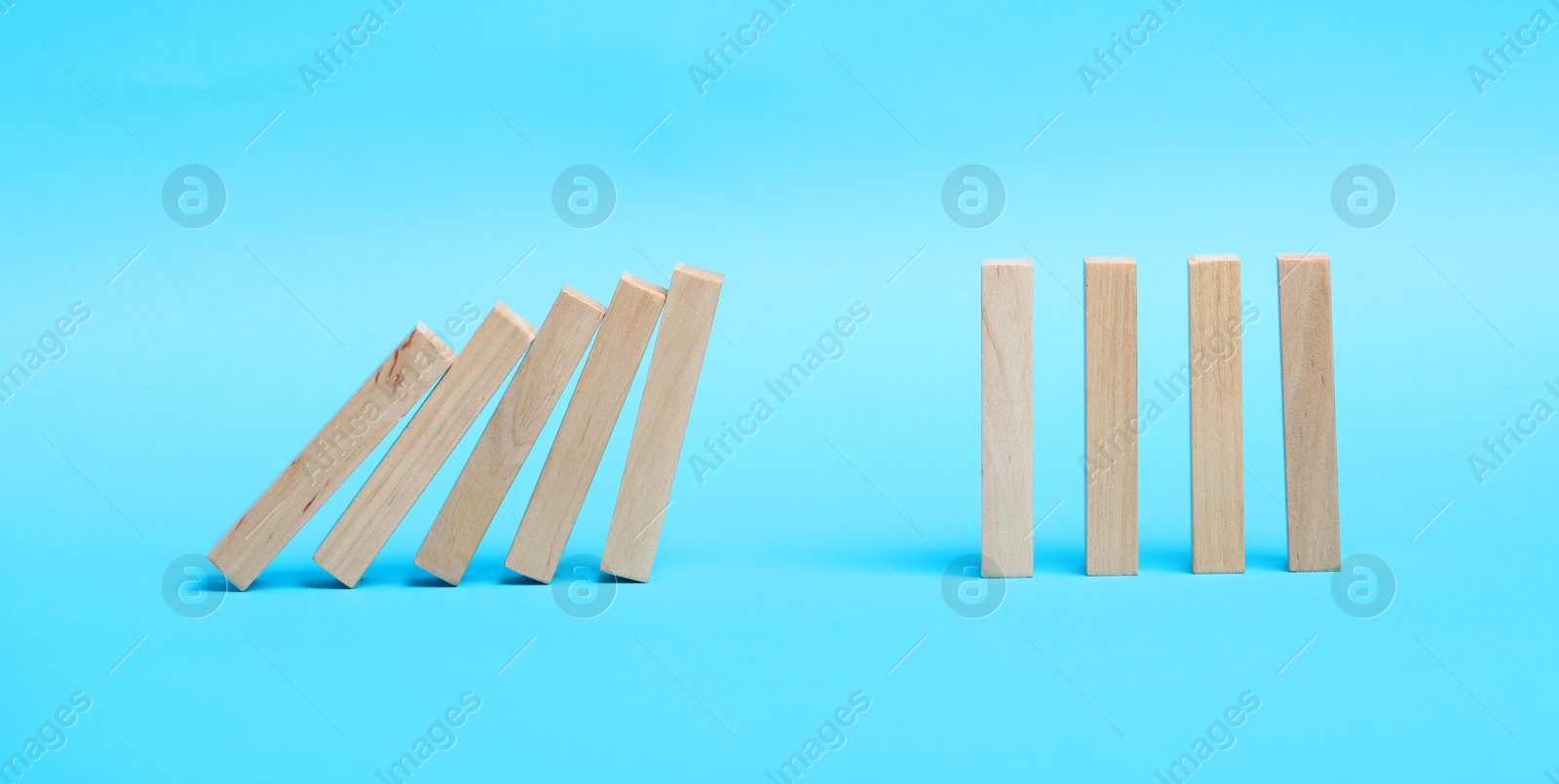 Photo of Domino effect. Wooden blocks falling on light blue background