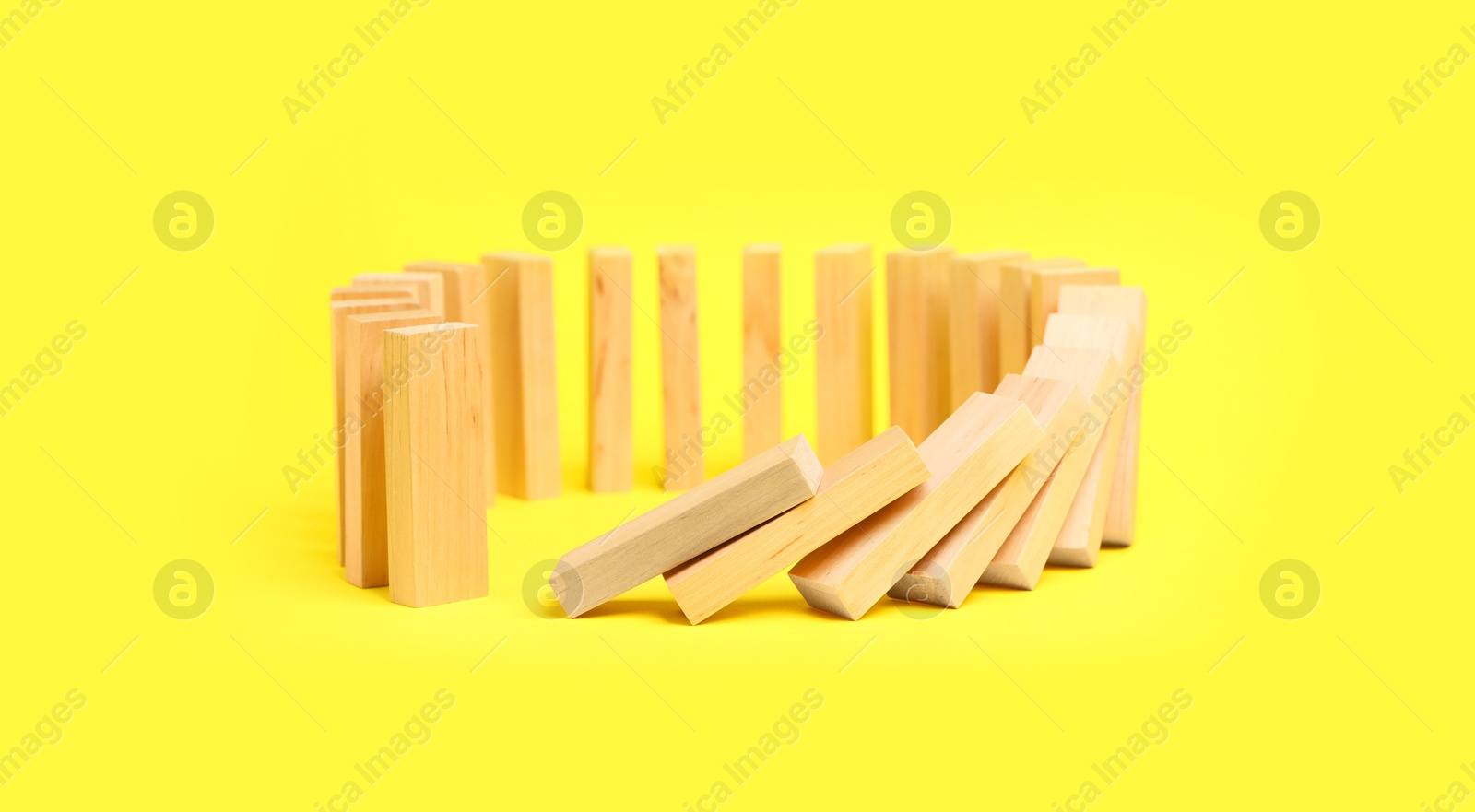 Photo of Domino effect. Wooden blocks falling on yellow background. Space for text