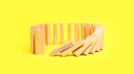 Photo of Domino effect. Wooden blocks falling on yellow background. Space for text