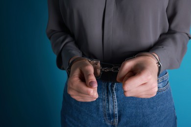 Photo of Woman in metal handcuffs on light blue background, closeup