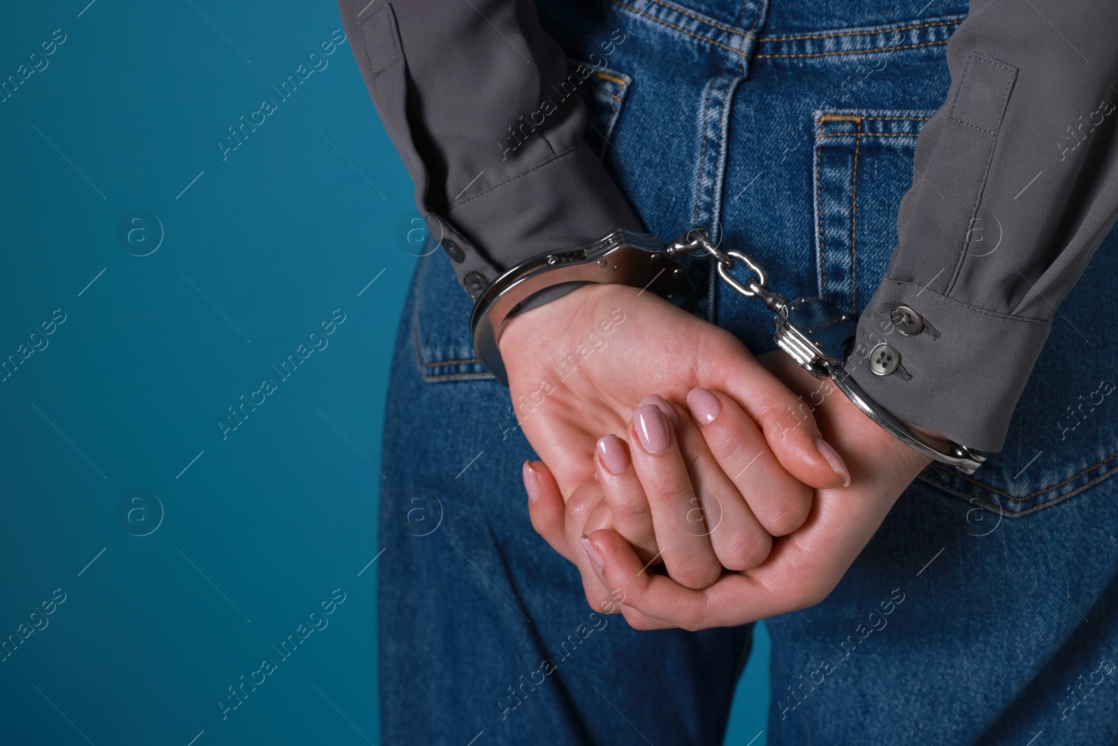 Photo of Woman in metal handcuffs on blue background, closeup. Space for text