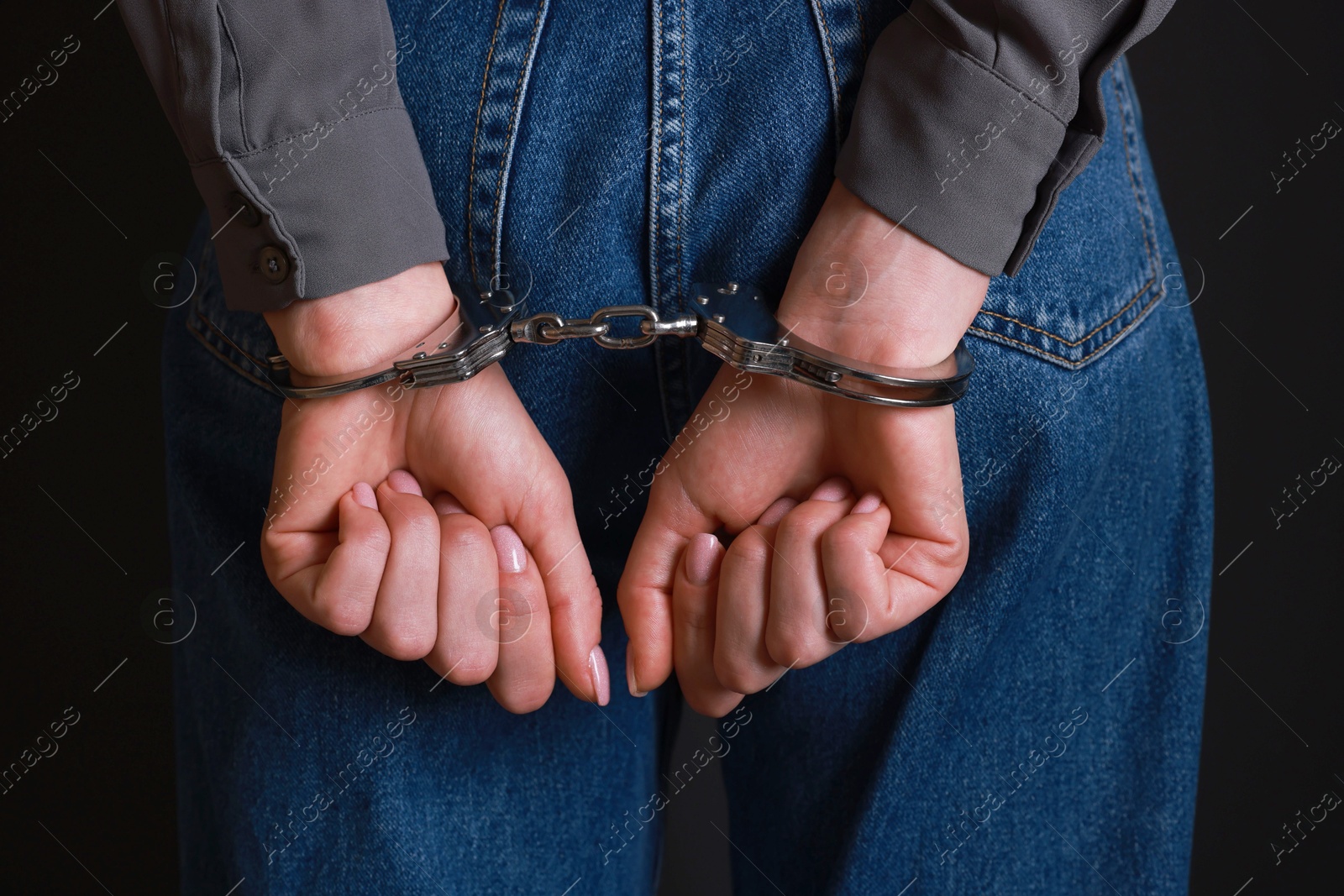 Photo of Woman in metal handcuffs on black background, closeup