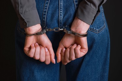 Photo of Woman in metal handcuffs on black background, closeup