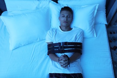 Photo of Sleepwalker fastened with belts lying on bed, top view