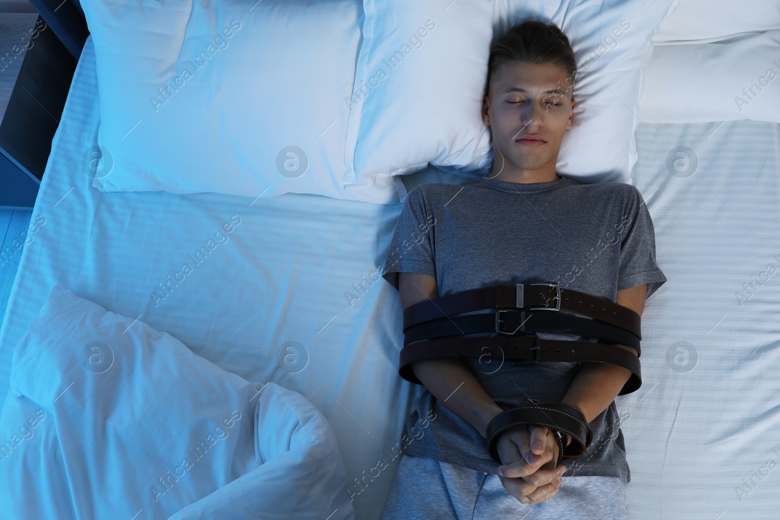 Photo of Sleepwalker fastened with belts lying on bed, top view