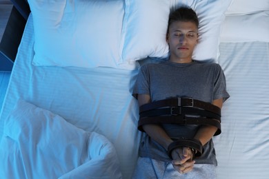 Photo of Sleepwalker fastened with belts lying on bed, top view