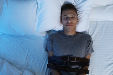 Photo of Sleepwalker fastened with belts lying on bed, top view