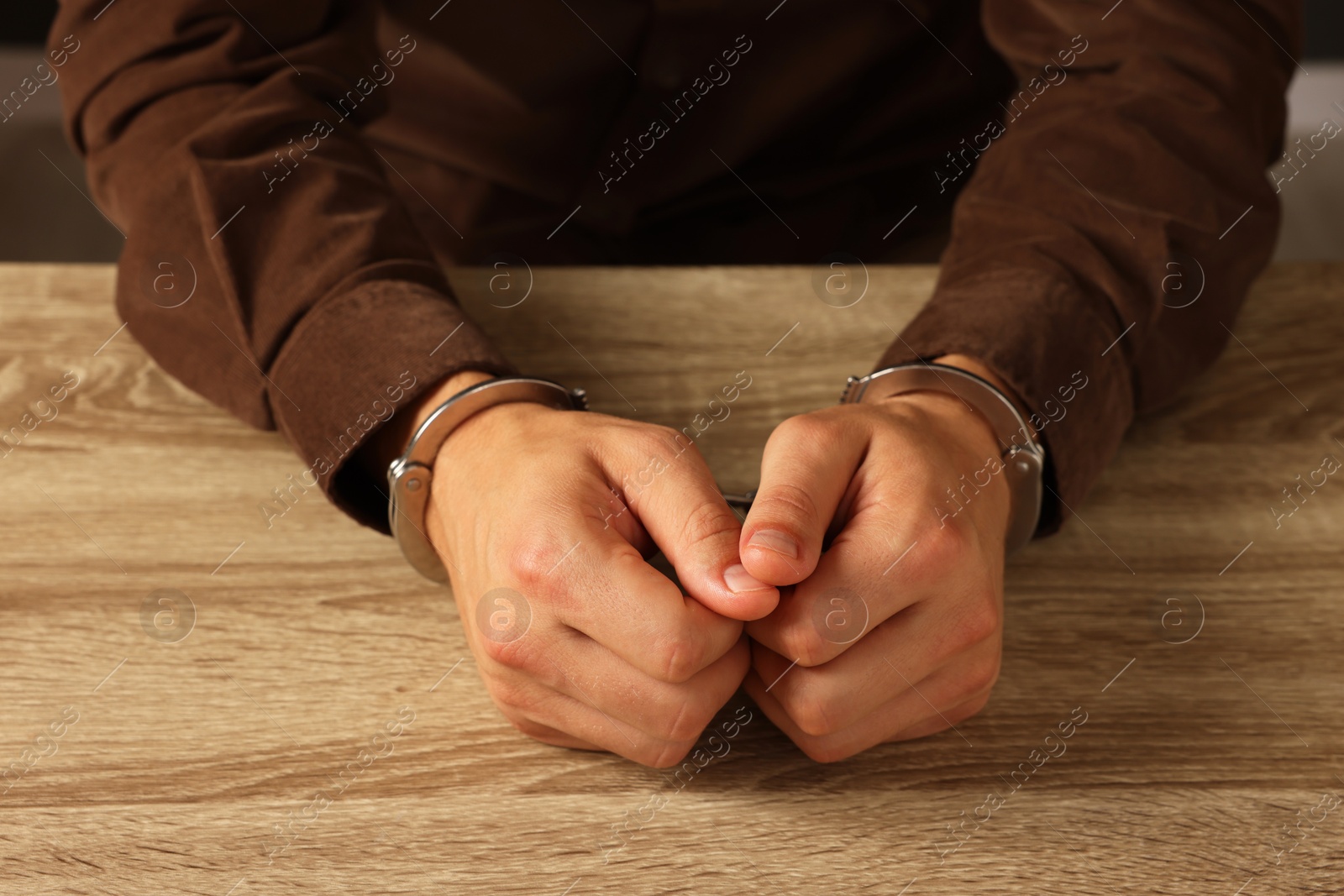 Photo of Man in metal handcuffs at wooden table, closeup