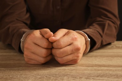 Photo of Man in metal handcuffs at wooden table, closeup