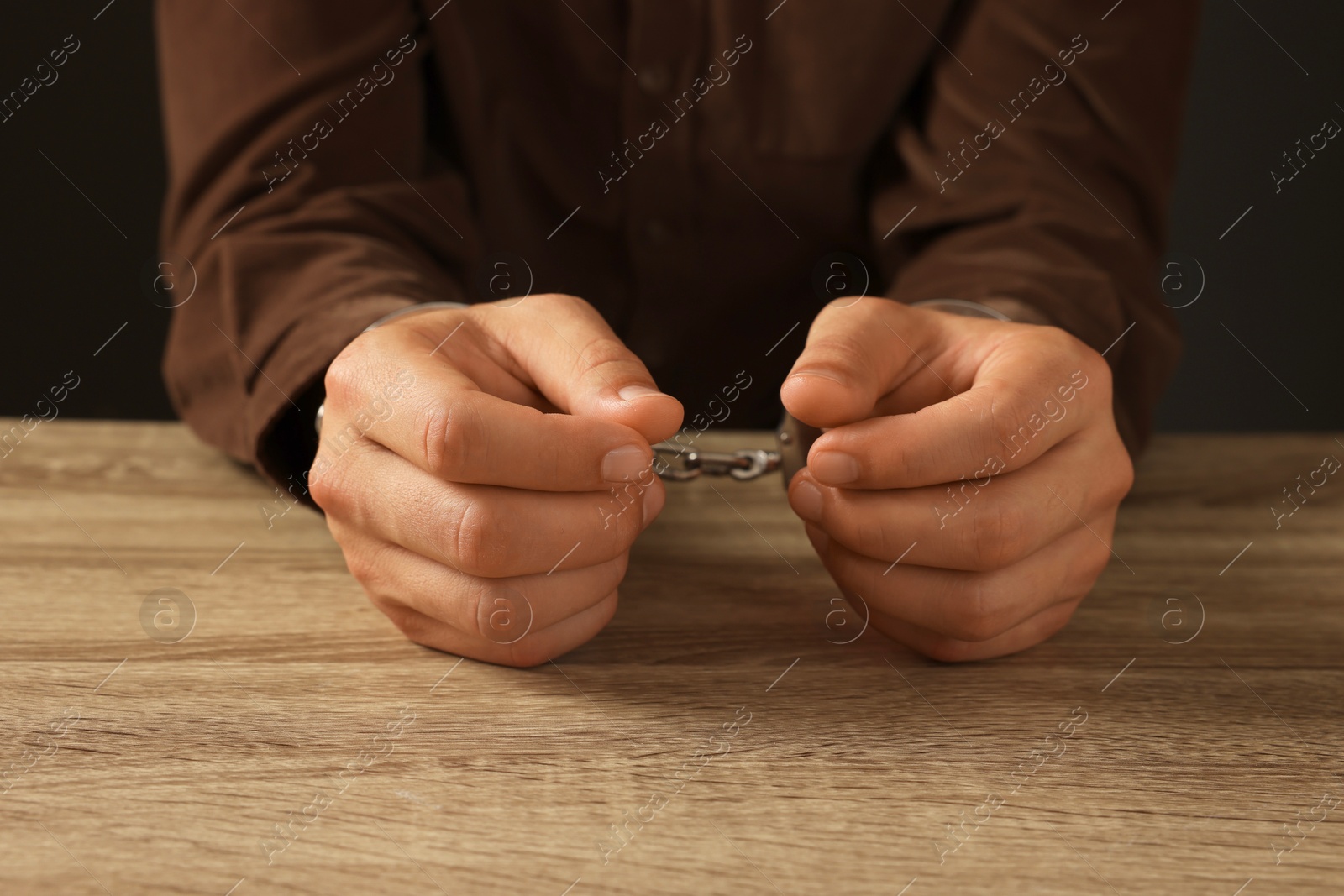 Photo of Man in metal handcuffs at wooden table, closeup