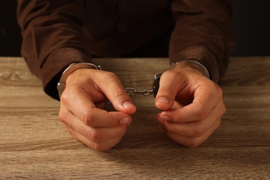 Photo of Man in metal handcuffs at wooden table, closeup