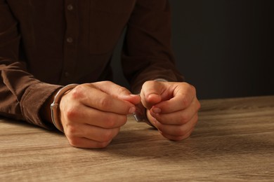 Photo of Man in metal handcuffs at wooden table against black background, closeup