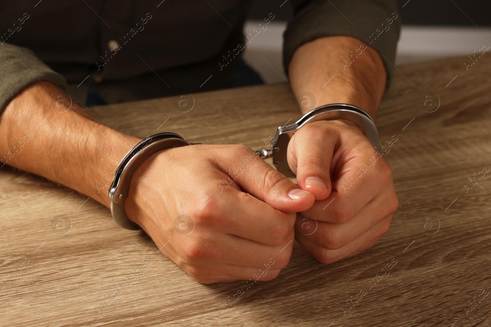 Photo of Man in metal handcuffs at wooden table, closeup