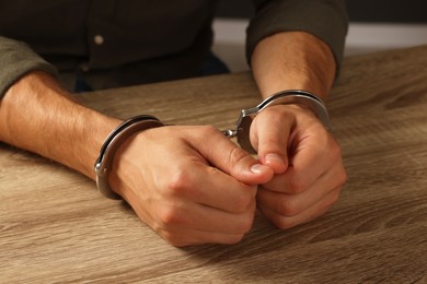 Man in metal handcuffs at wooden table, closeup