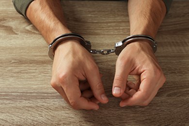 Photo of Man in metal handcuffs at wooden table, closeup