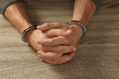 Photo of Man in metal handcuffs at wooden table, closeup