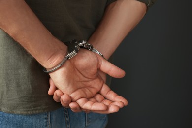 Photo of Man in metal handcuffs on black background, closeup. Space for text