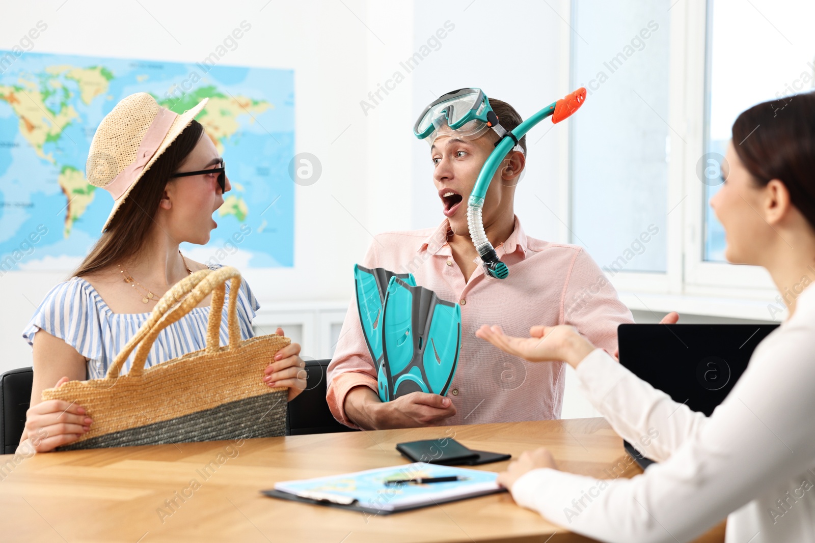 Photo of Happy couple planning vacation with travel agent at wooden table in office