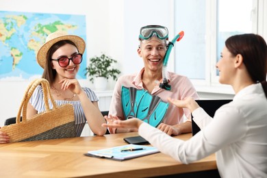 Photo of Happy couple planning vacation with travel agent at wooden table in office