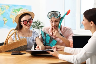 Happy couple planning vacation with travel agent at wooden table in office