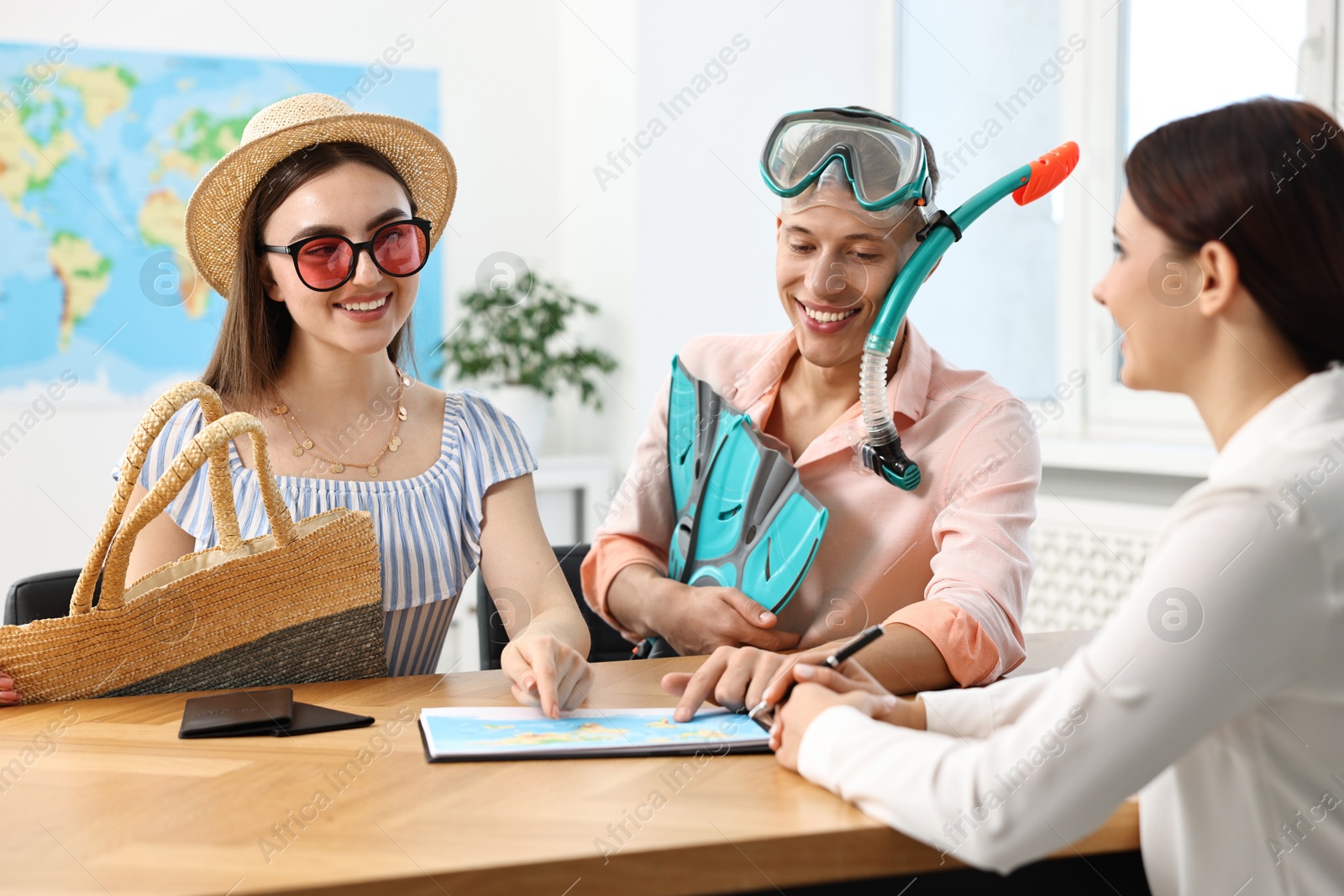 Photo of Happy couple planning vacation with travel agent at wooden table in office