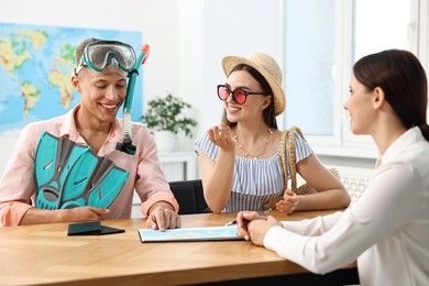 Photo of Happy couple planning vacation with travel agent at wooden table in office