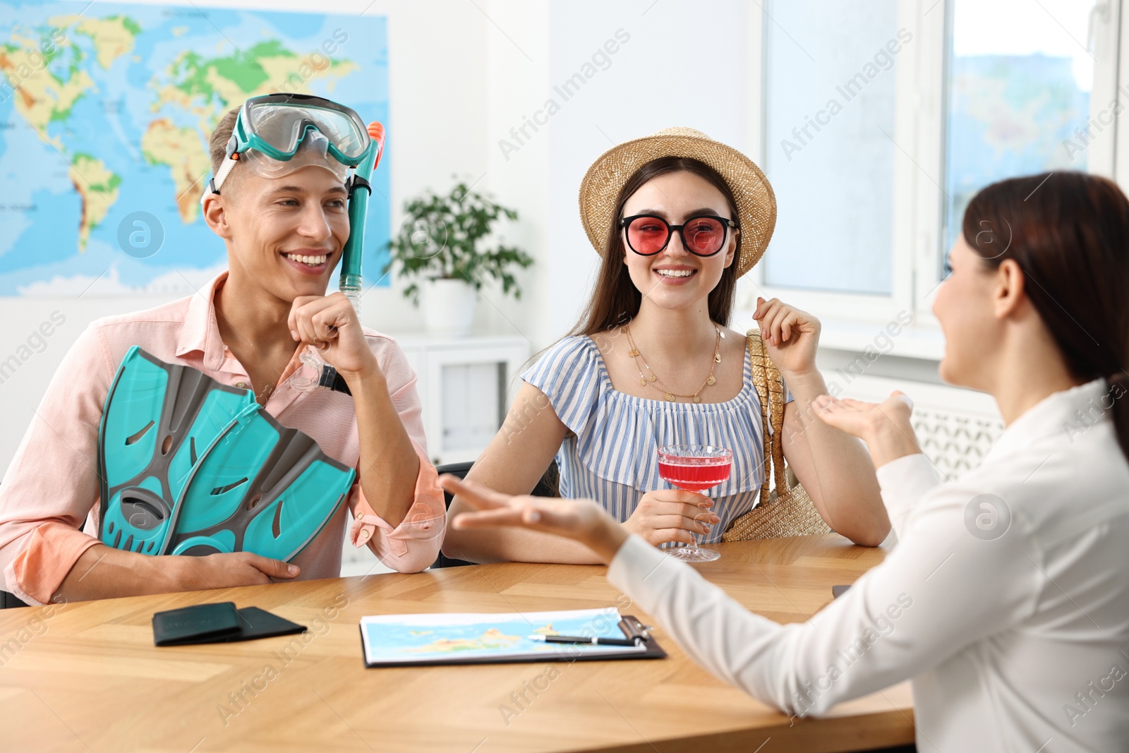 Photo of Happy couple planning vacation with travel agent at wooden table in office