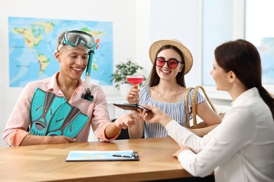 Happy couple planning vacation with travel agent at wooden table in office