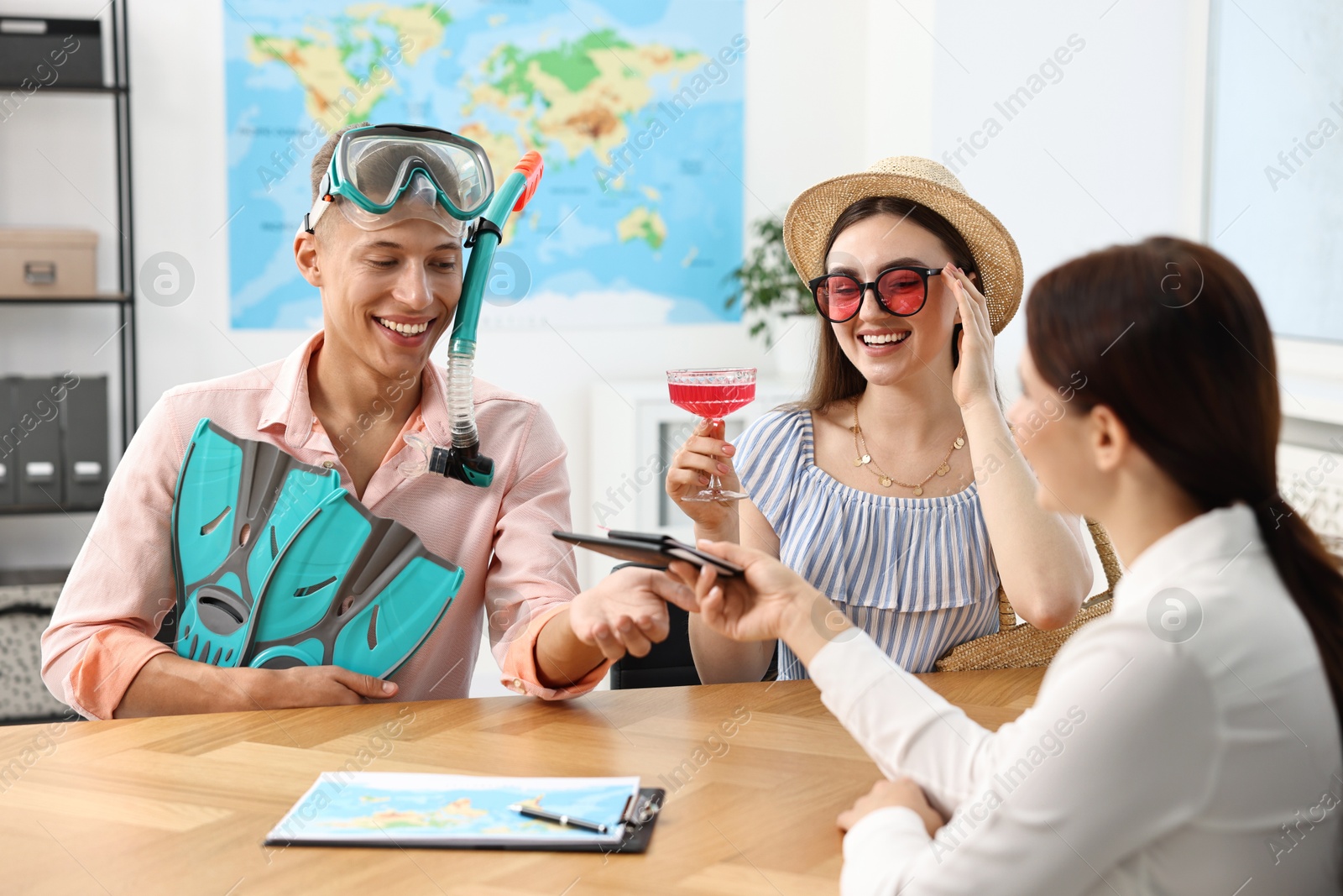 Photo of Happy couple planning vacation with travel agent at wooden table in office