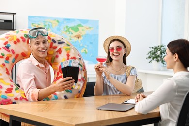 Photo of Happy couple planning vacation with travel agent at wooden table in office