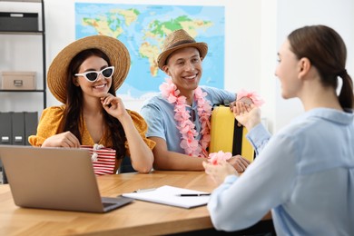 Photo of Happy couple planning vacation with travel agent at wooden table in office