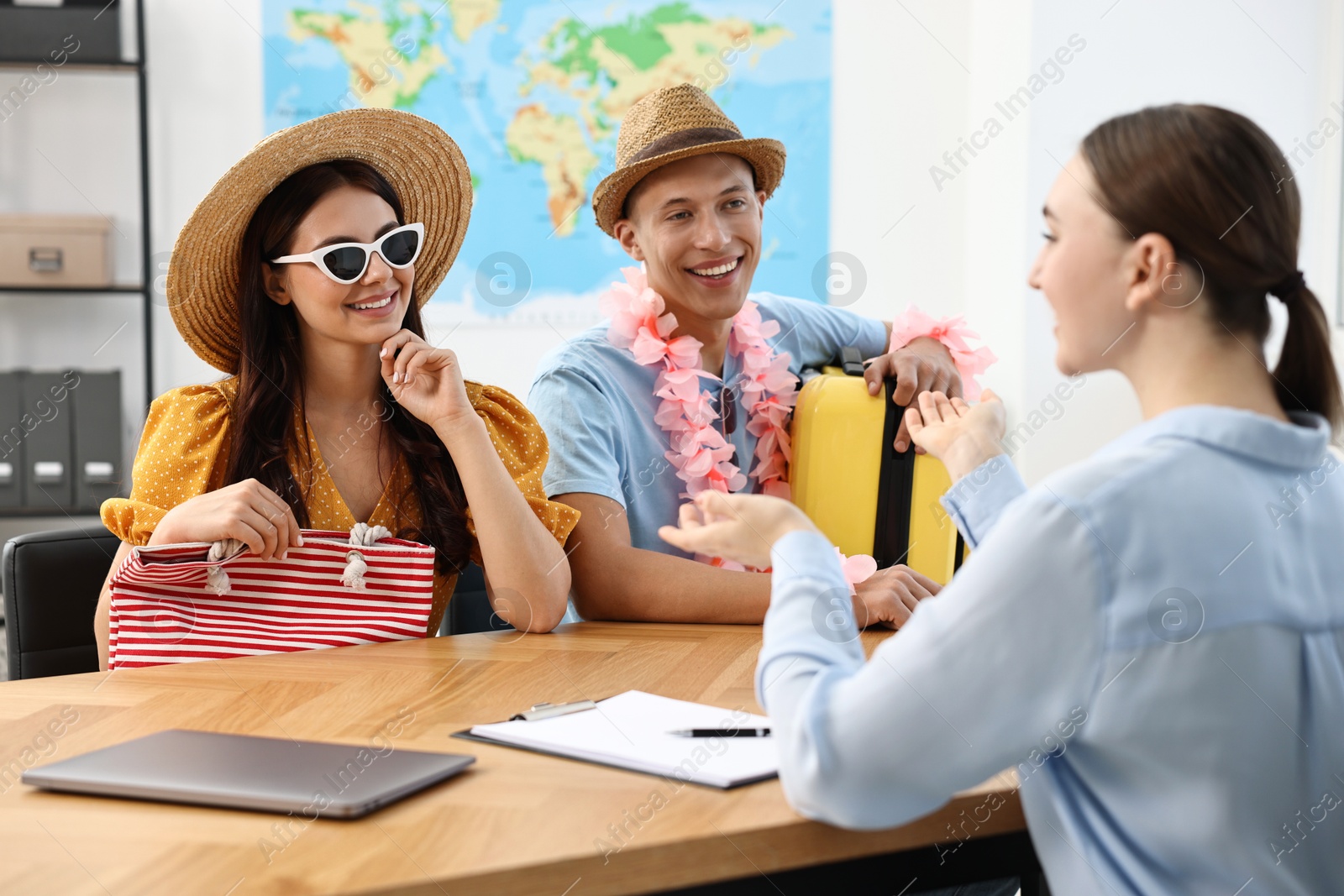 Photo of Happy couple planning vacation with travel agent at wooden table in office