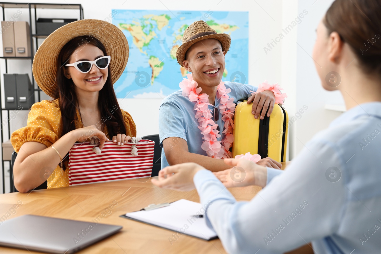 Photo of Happy couple planning vacation with travel agent at wooden table in office