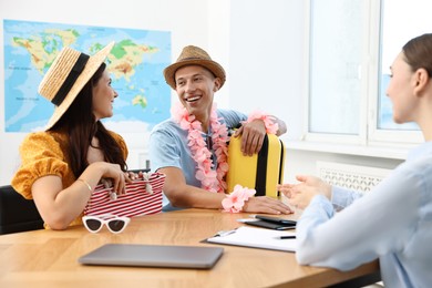 Photo of Happy couple planning vacation with travel agent at wooden table in office