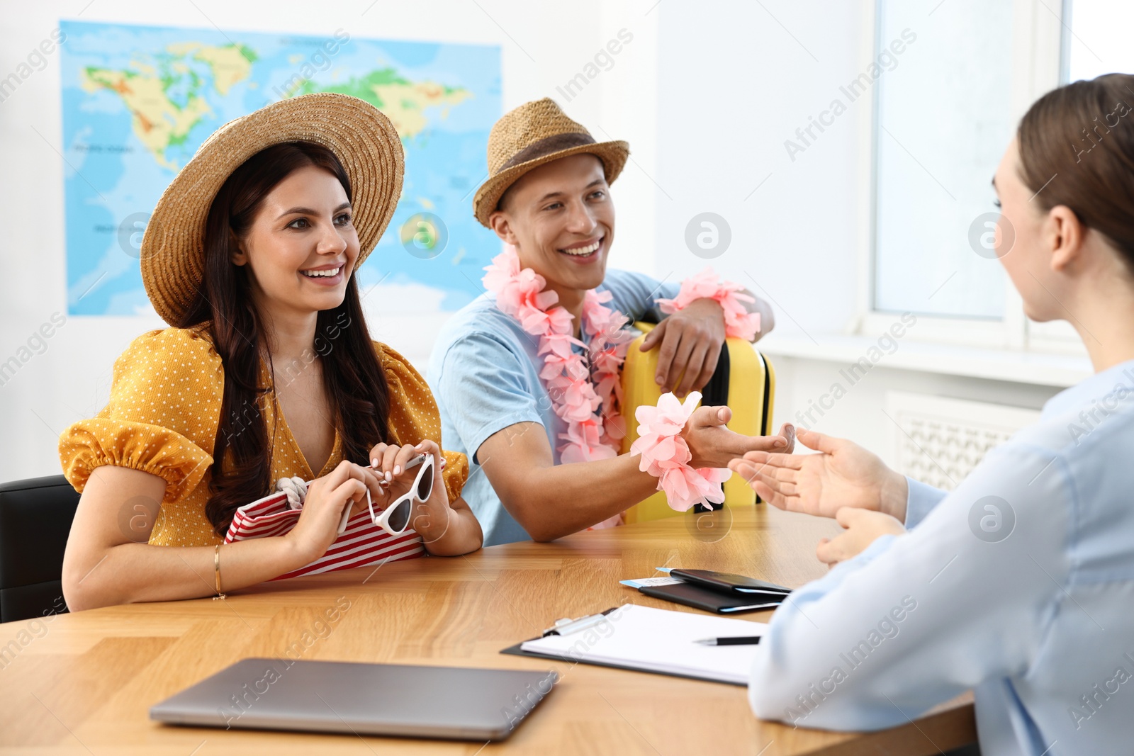 Photo of Happy couple planning vacation with travel agent at wooden table in office