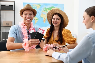 Happy couple planning vacation with travel agent at wooden table in office