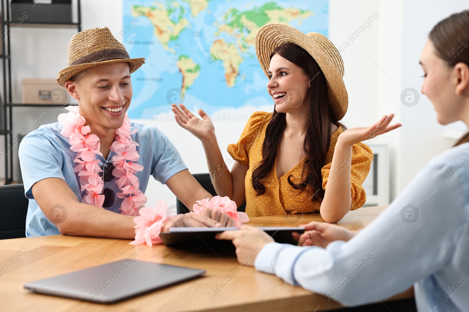 Photo of Happy couple planning vacation with travel agent at wooden table in office