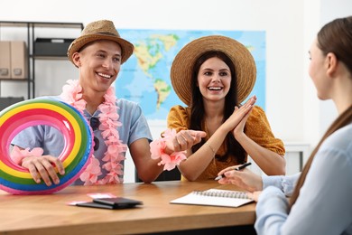 Photo of Happy couple planning vacation with travel agent at wooden table in office