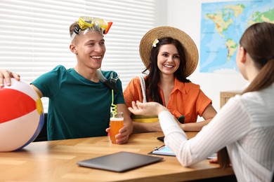 Happy couple planning vacation with travel agent at wooden table in office