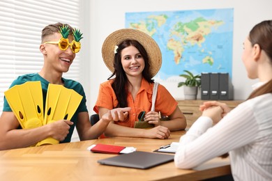 Photo of Happy couple planning vacation with travel agent at wooden table in office