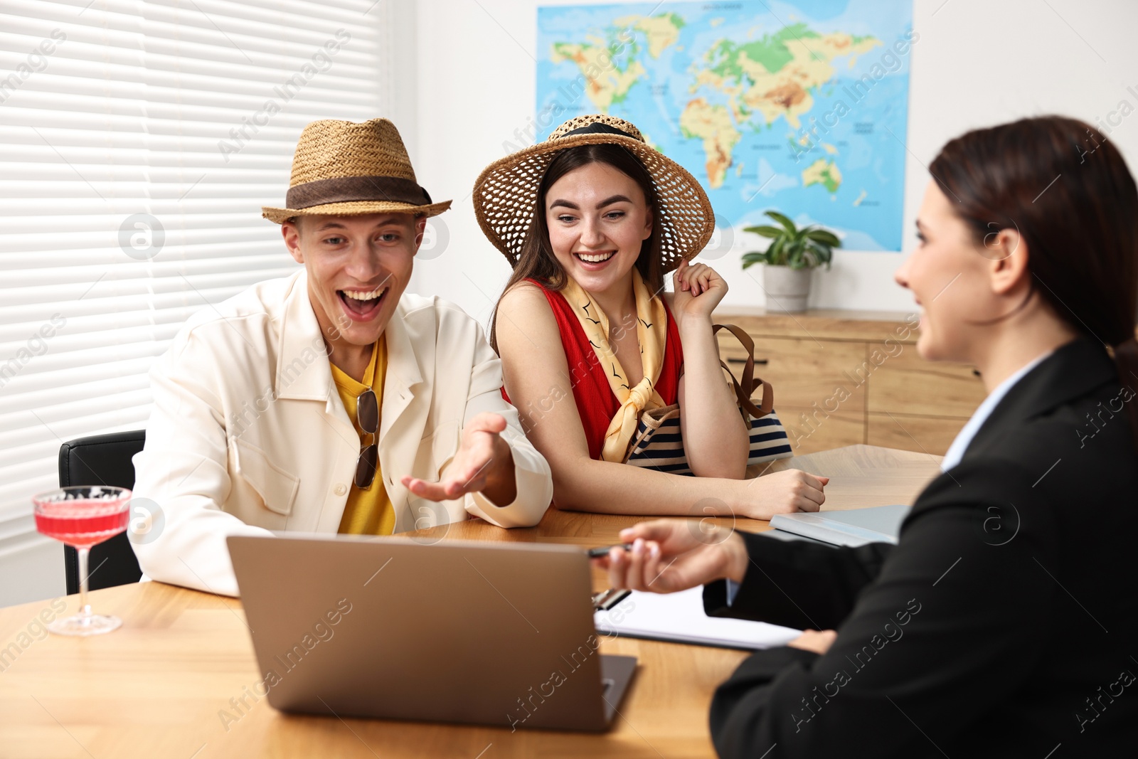 Photo of Happy couple planning vacation with travel agent at wooden table in office