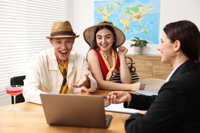 Happy couple planning vacation with travel agent at wooden table in office