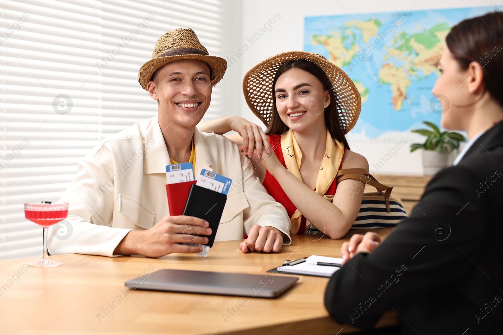 Photo of Happy couple planning vacation with travel agent at wooden table in office