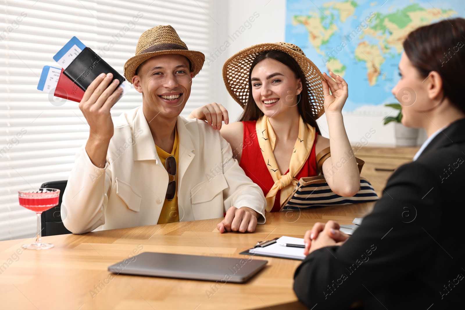 Photo of Happy couple planning vacation with travel agent at wooden table in office