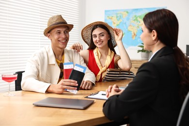 Photo of Happy couple planning vacation with travel agent at wooden table in office