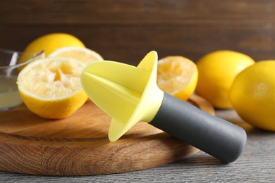 Photo of Plastic juicer and fresh lemons on grey wooden table, closeup