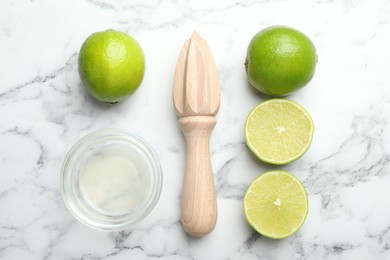 Photo of Wooden juicer and fresh limes on white marble table, flat lay